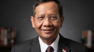 Potret Prof. Dr. Mahfud MD mengenakan jas dengan latar belakang koleksi buku