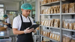 Petugas usaha pangan olahan memeriksa dokumen Sertifikasi Keamanan Pangan Mandiri di ruang produksi